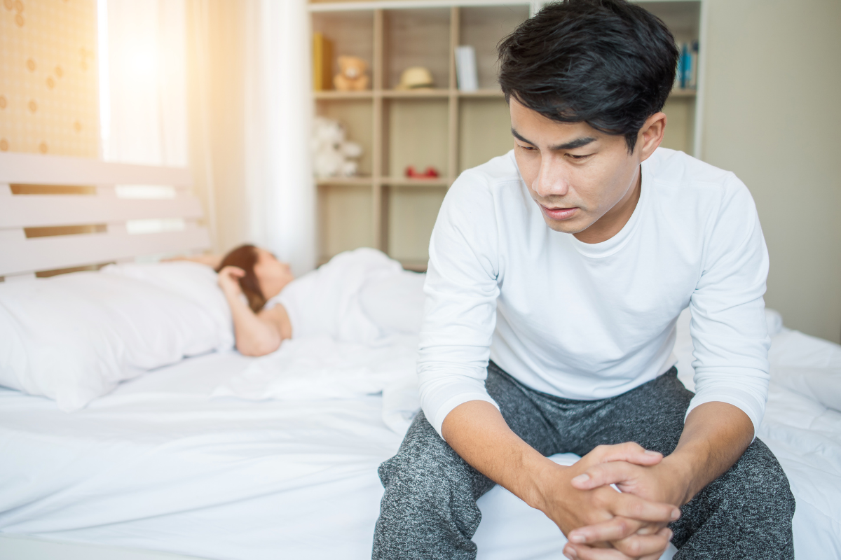 Orang yang terduduk di samping tempat tidur sambil merasa sedih